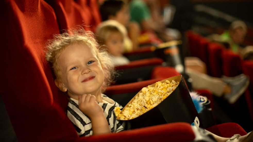 Curly haired girl sitting in a cinema looking very happy with a bucket of popcorn in her lap